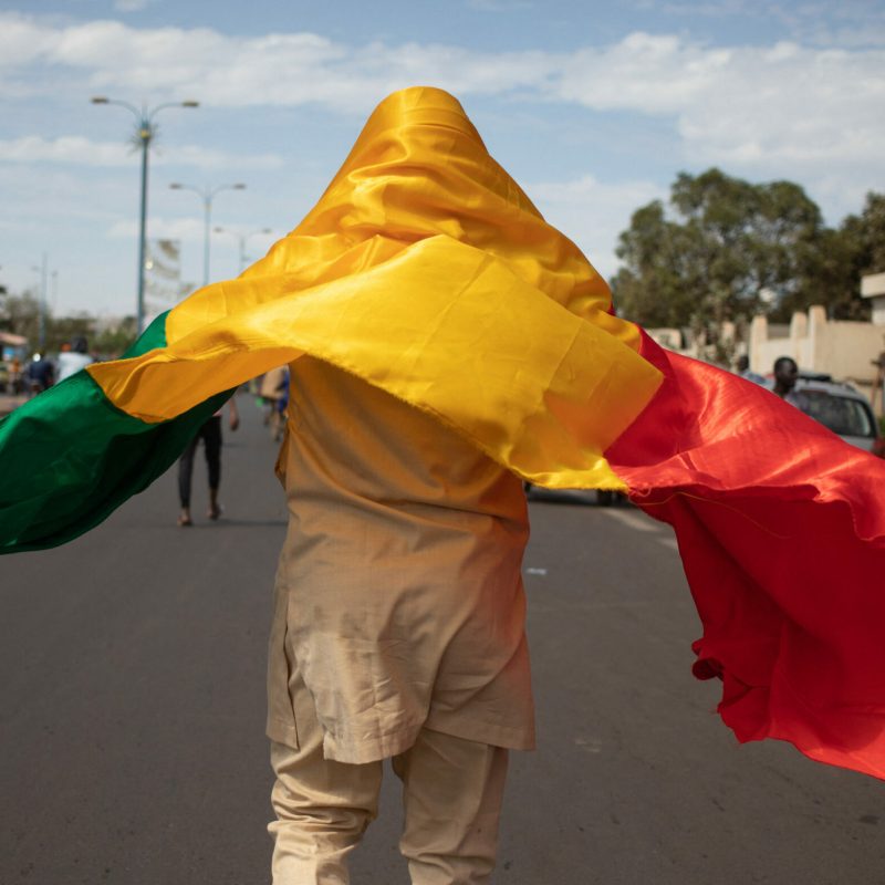 A man with the Malian National flag draped over his head and shoulders joins a mass demonstration in Bamako on 14 January 2022 to protest against sanctions imposed on Mali and the Junta by the Economic Community of West African States (ECOWAS).